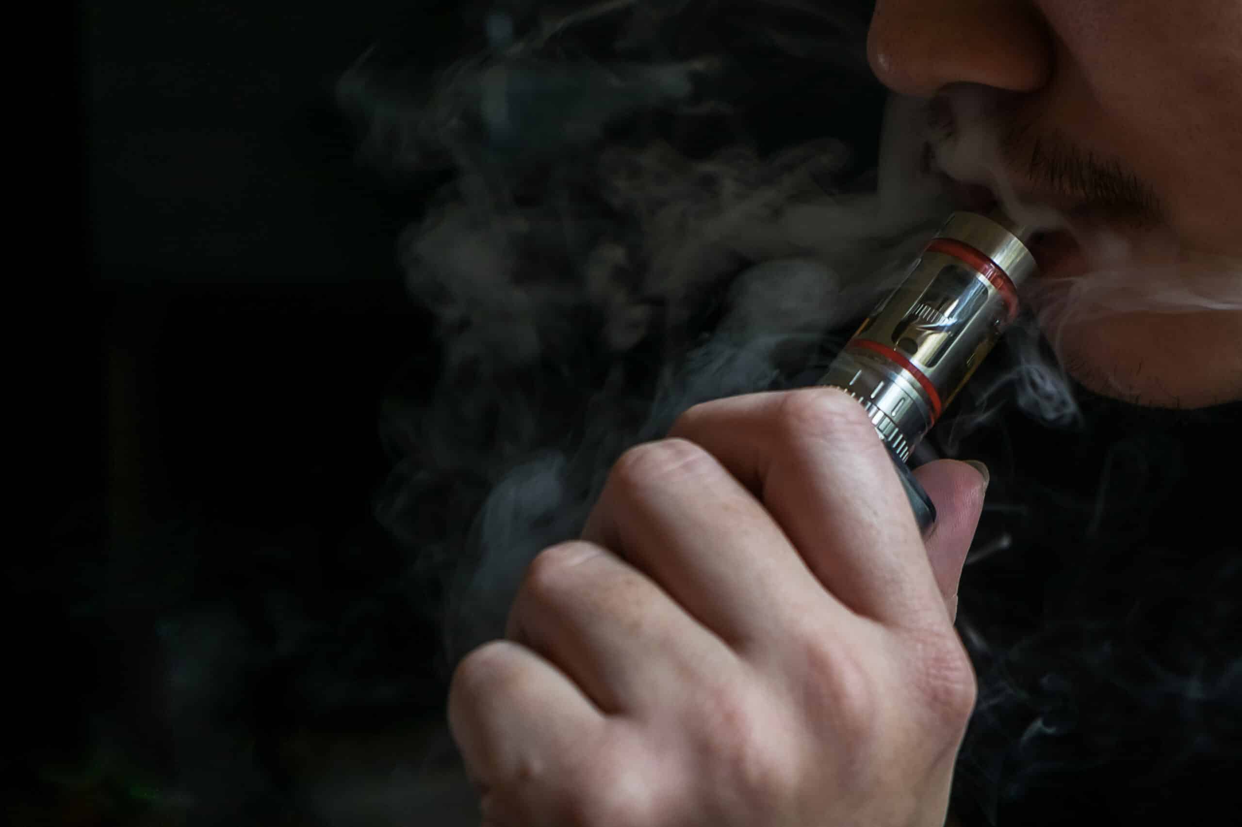 Man with concealed identity smoking a controversial vaping an electronic cigarette. Vaping is debatable in the health community if it is safe or a health risk