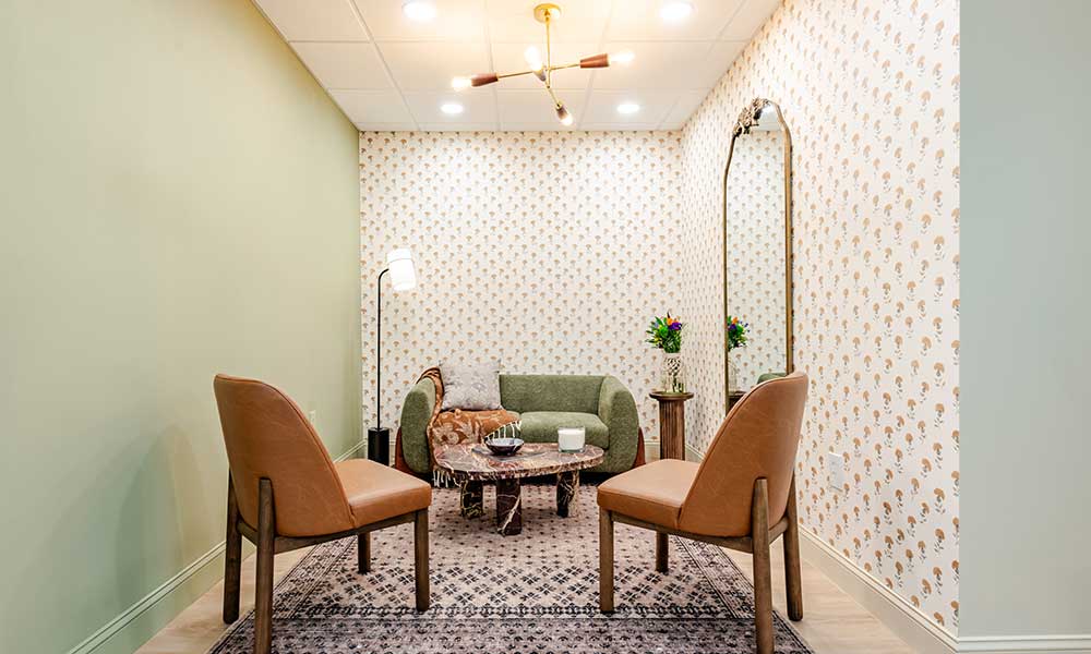 Room with two brown chairs, a green sofa, patterned wallpaper, floor lamp, and decorative mirror.