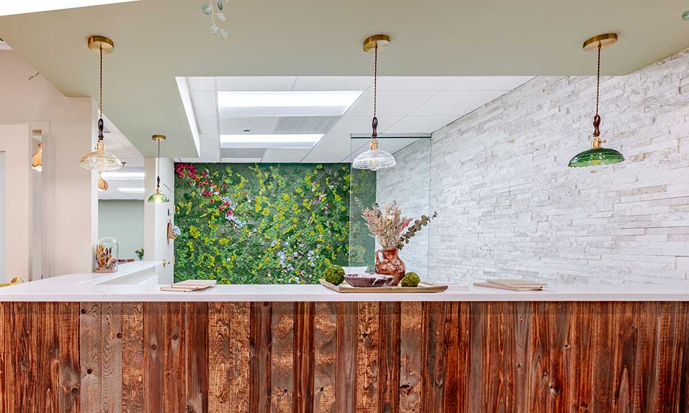 Reception area with wooden counter, pendant lights, and a green plant wall.