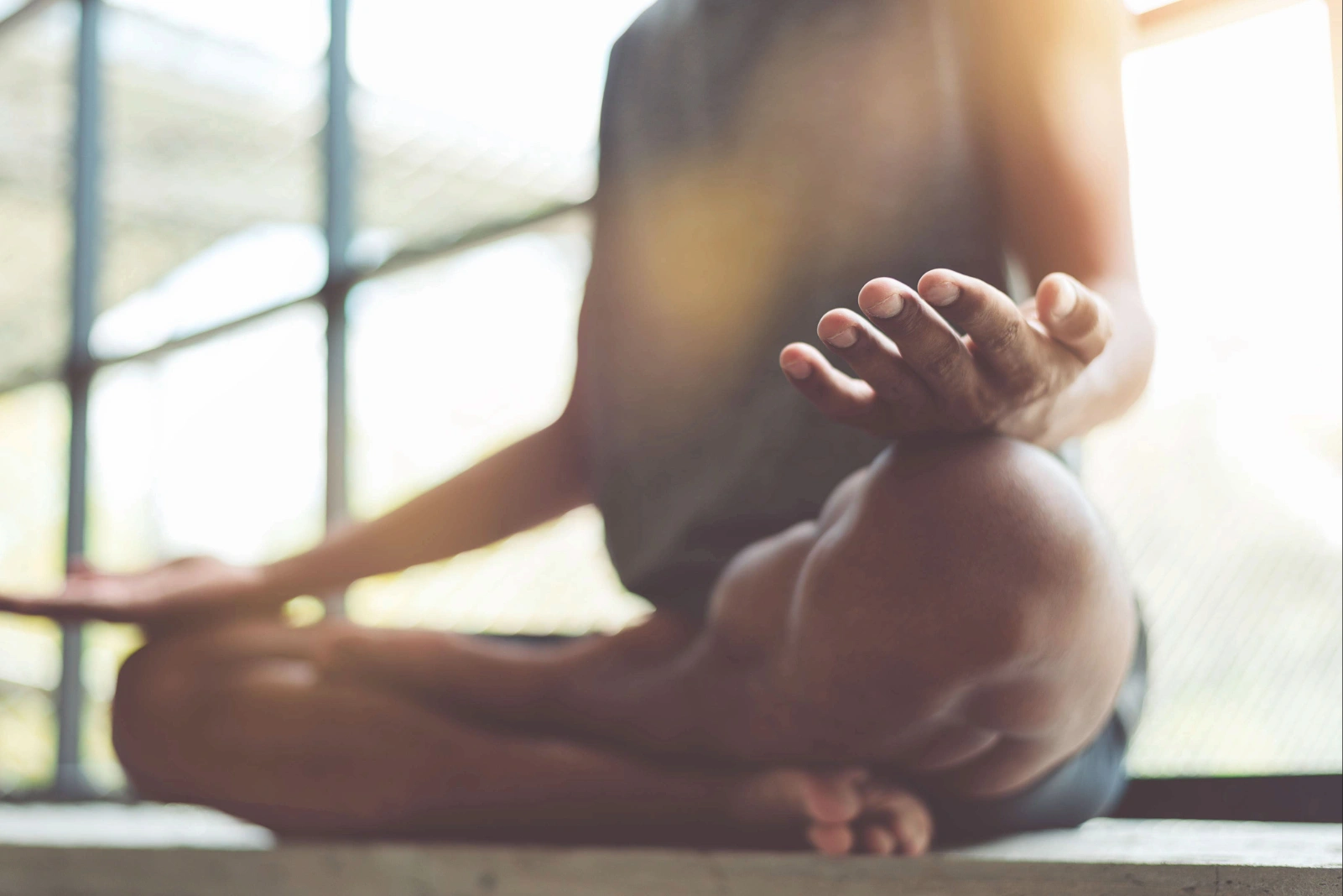 Person sitting cross-legged meditating, with hand resting on knee in soft light.