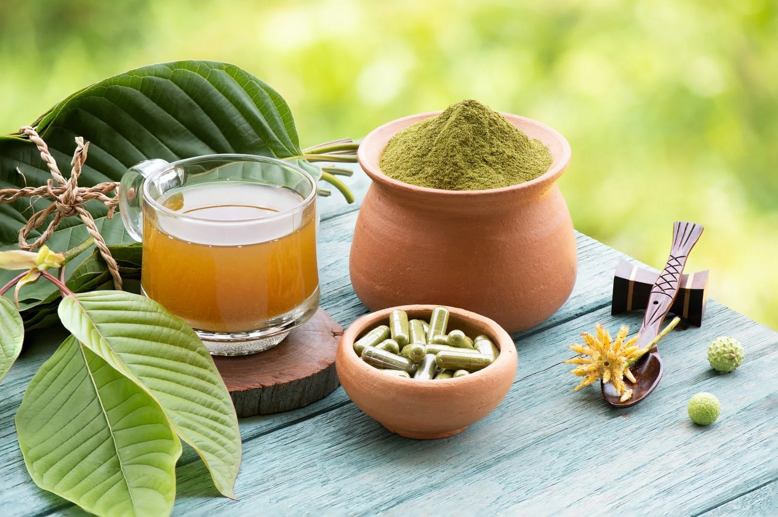 Kratom Toxicity: Herbal ingredients with green powder and capsules on blue wooden table.