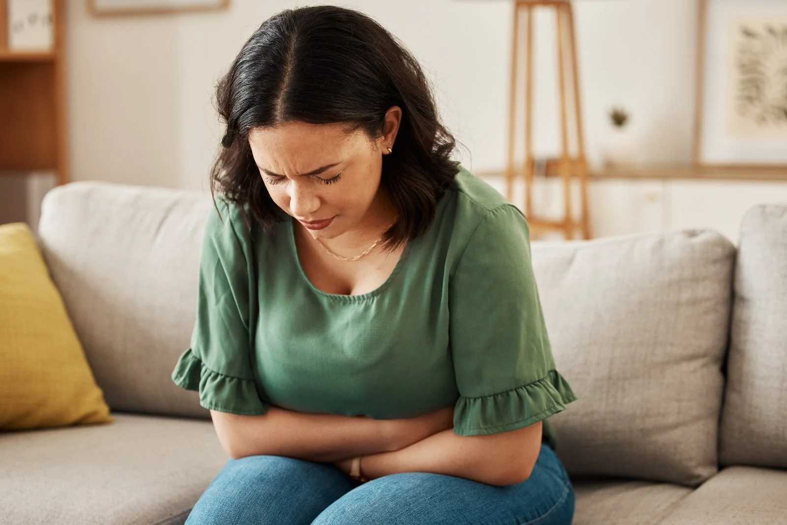 Side Effects of Laudanum: Person in green blouse sitting on sofa holding stomach.