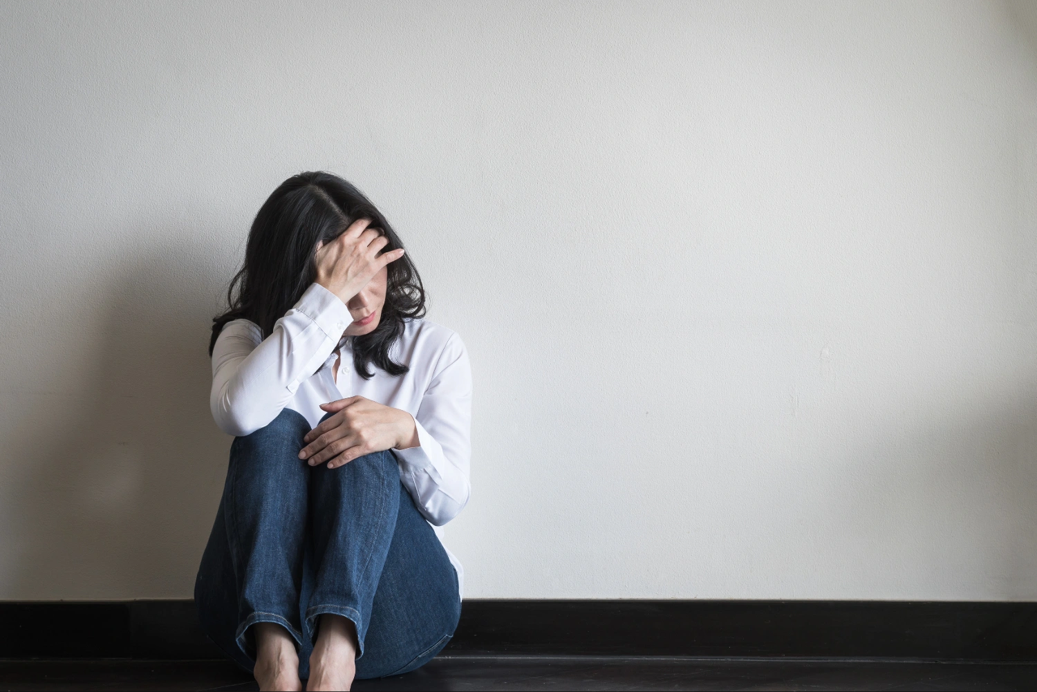 Person sitting with hand on forehead, wearing white shirt and jeans.